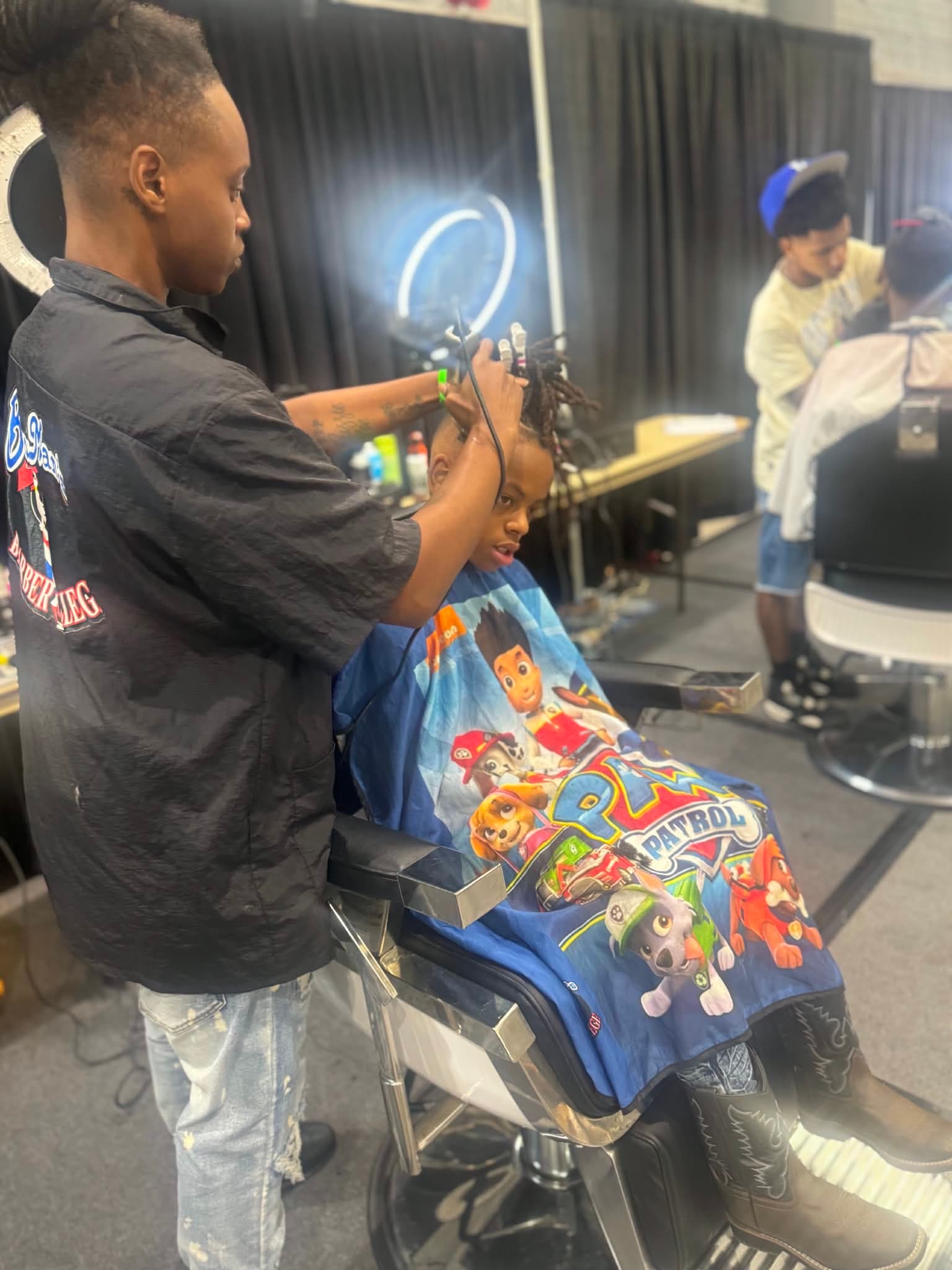 Barbers work side-by-side stations, one cutting a young client, during B²E² 2026.